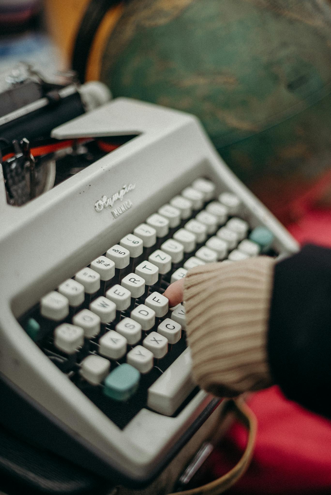 About 2 Close-up of a person's hand typing on a vintage Olympia typewriter, evoking nostalgia and craftsmanship.